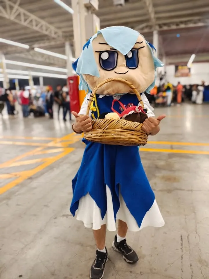 A person in a full-body costume of the anime character Rem from Re:Zero, holding a wicker basket and giving thumbs up…