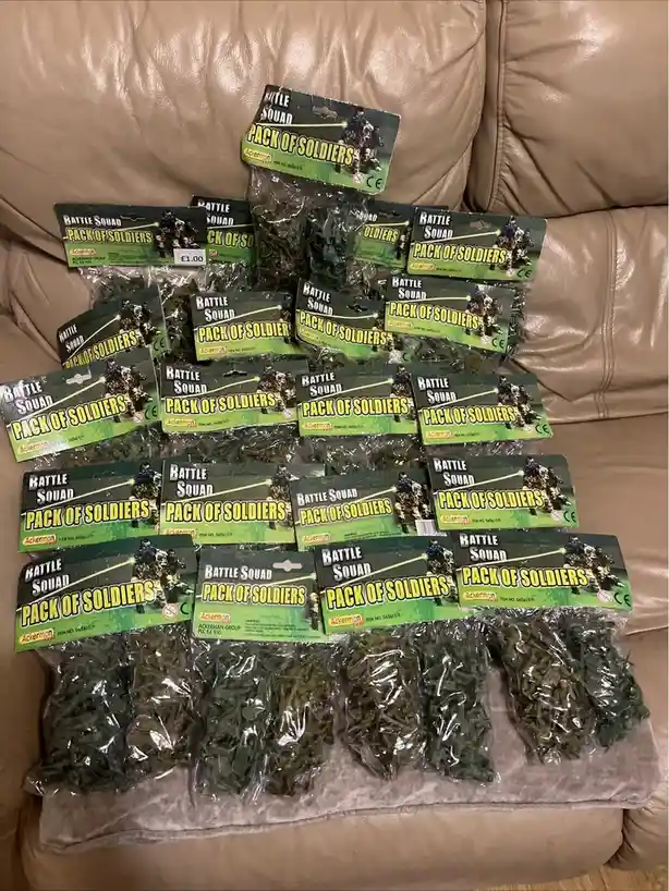 Multiple identical plastic packages labeled 'Battle Squad Pack of Soldiers' by Ackerman are arranged in rows on a tan…