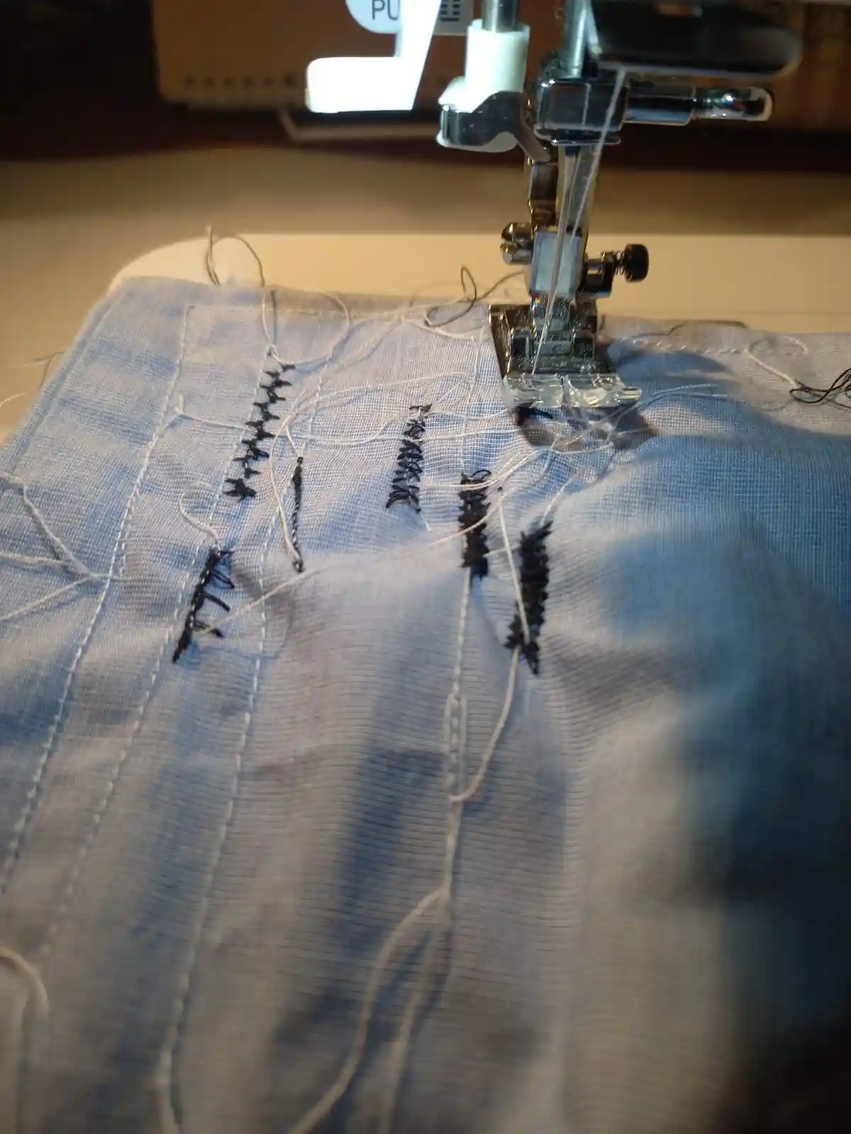 A close-up photo shows a sewing machine needle poised over light blue fabric, which has several messy, uneven rows of black…