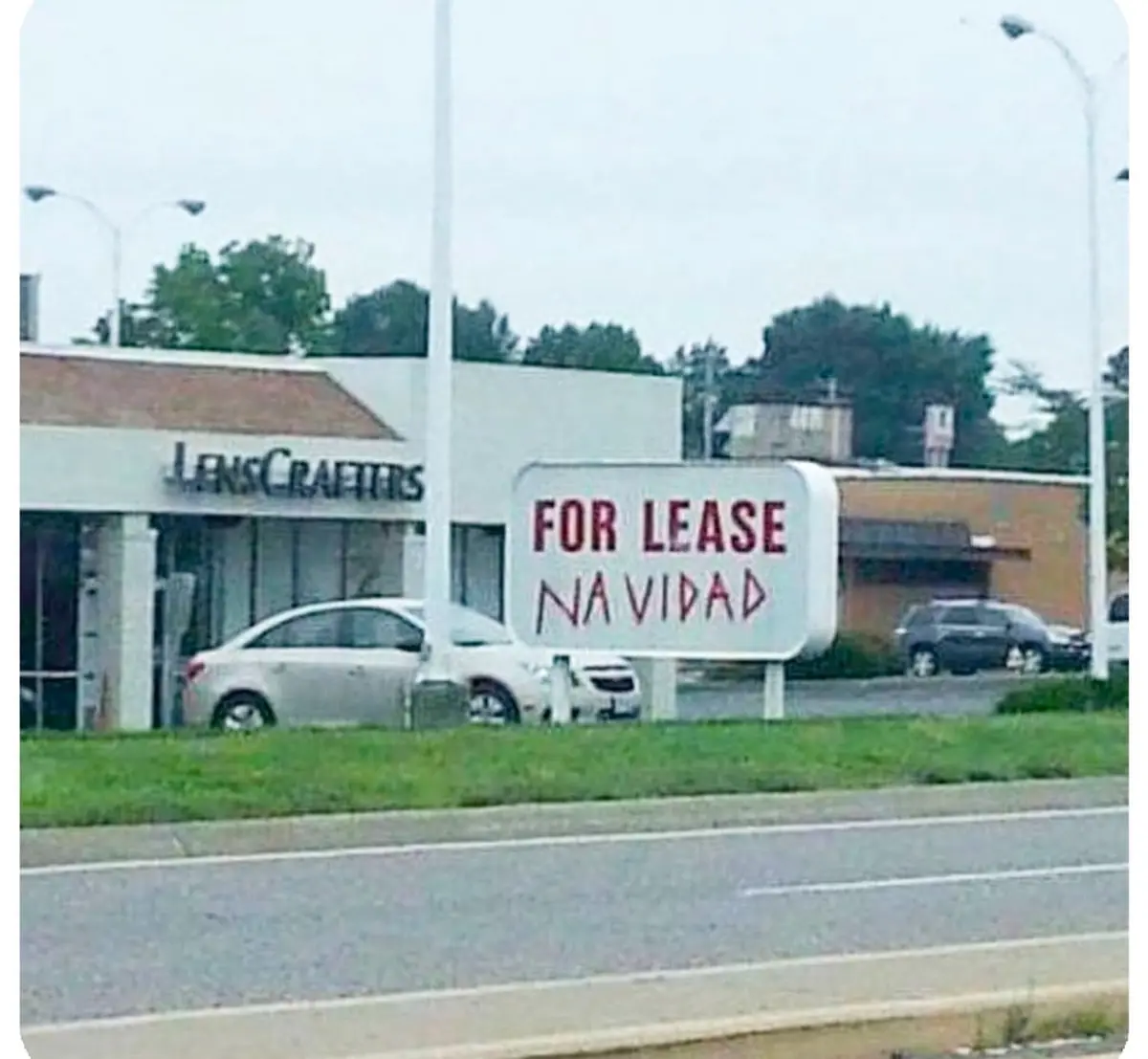 A blurry outdoor photo shows a 'FOR LEASE' sign with 'NAVIDAD' handwritten underneath in red marker, placed in front of a…