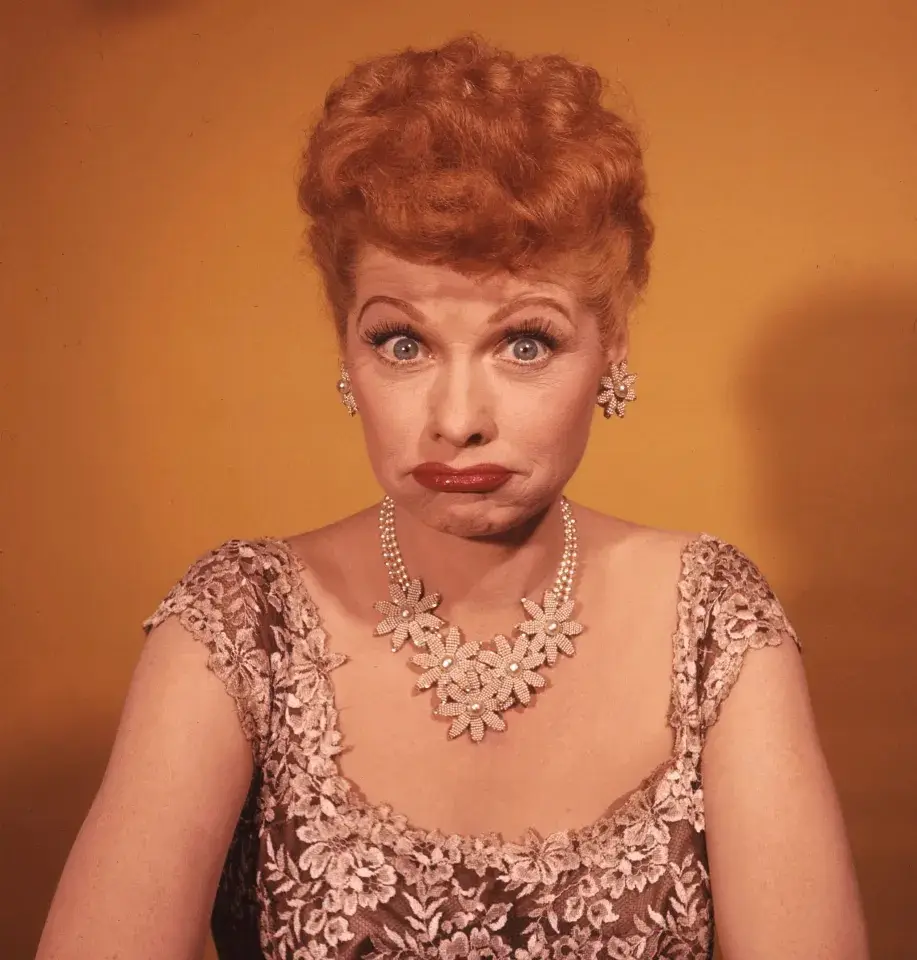 A vintage portrait of actress Lucille Ball with wide, shocked eyes and a downturned mouth, wearing a floral-patterned dress…