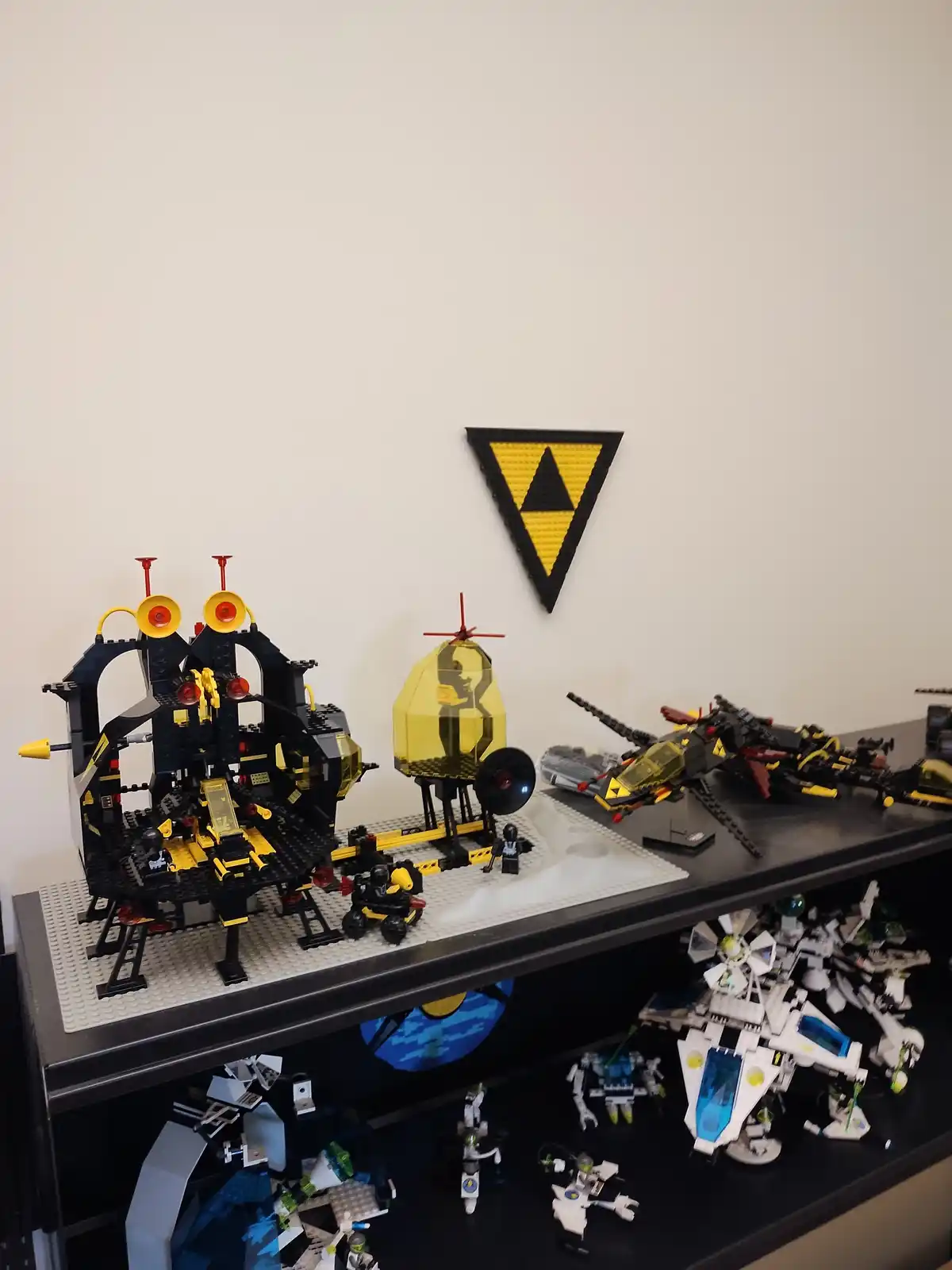 A shelf displays a collection of black and yellow Lego models, including a large base, a transparent dome, and several…