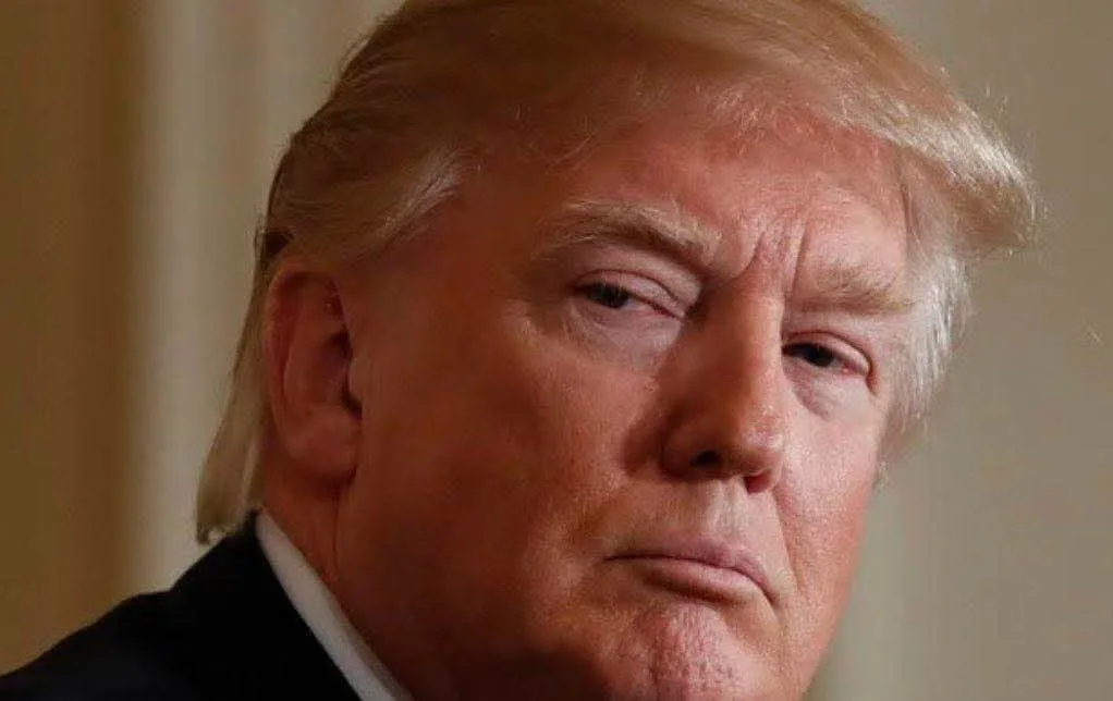 a close-up photo of former president donald trump with a stern, unimpressed facial expression, looking slightly to his…