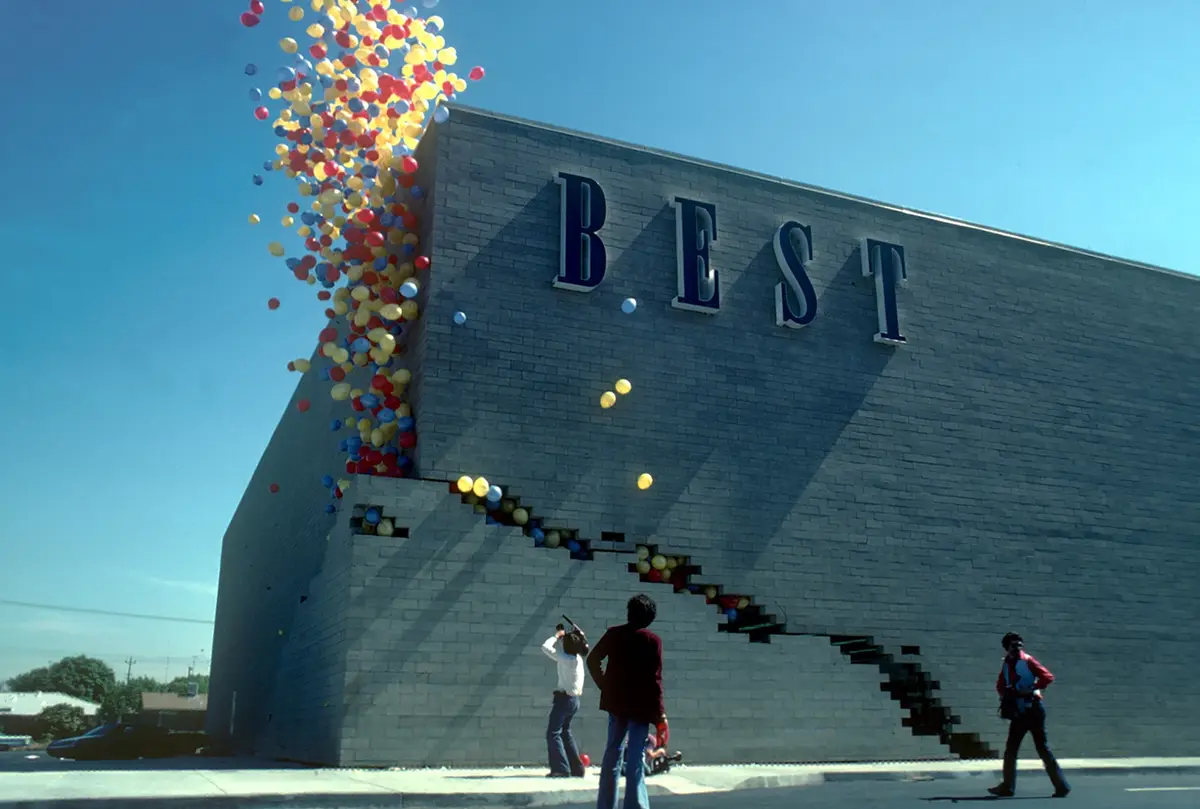 A vintage photo shows a gray brick building with the word 'BEST' in large blue letters. A cascade of red, yellow, and blue…