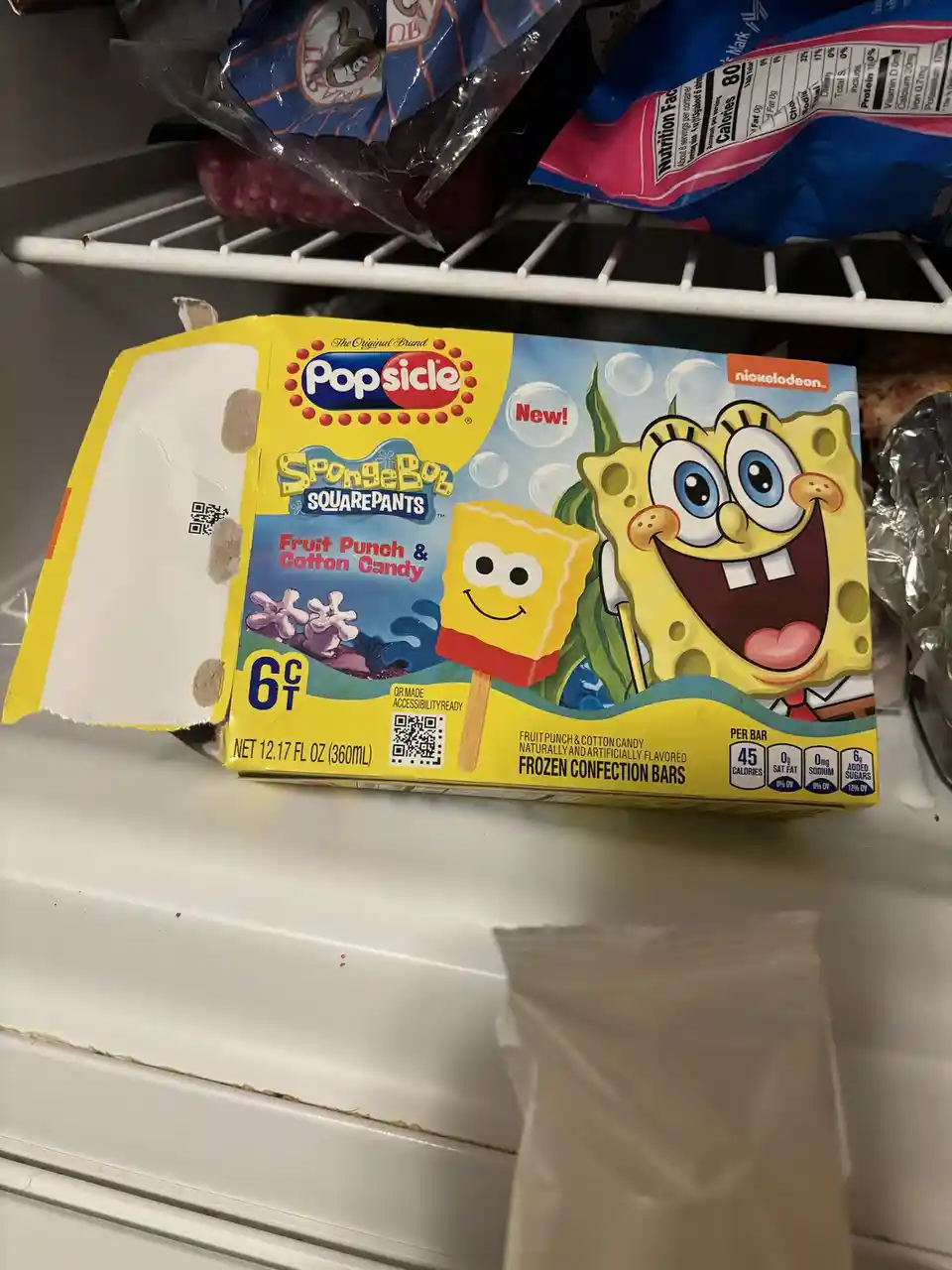 A partially opened box of SpongeBob SquarePants themed Popsicle frozen confection bars sits on a freezer shelf, with the…