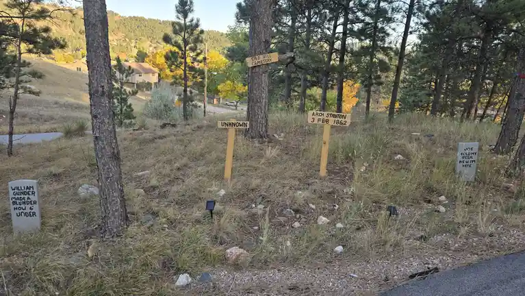 A photo of a small, rustic cemetery called 'Sad Hill Cemetery' with several handmade wooden and stone grave markers. One…