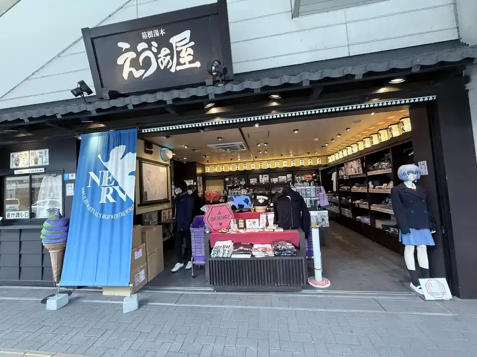 A storefront with a large blue banner displaying the NERV logo and slogan 'GONZAN HIS HEAVEN. ALL'S RIGHT WITH THE WORLD.'…