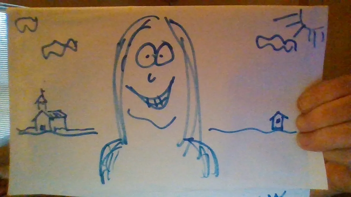 A hand holds up a child's blue ink drawing on paper showing a large smiling ghost-like figure with long hair and hands, with…