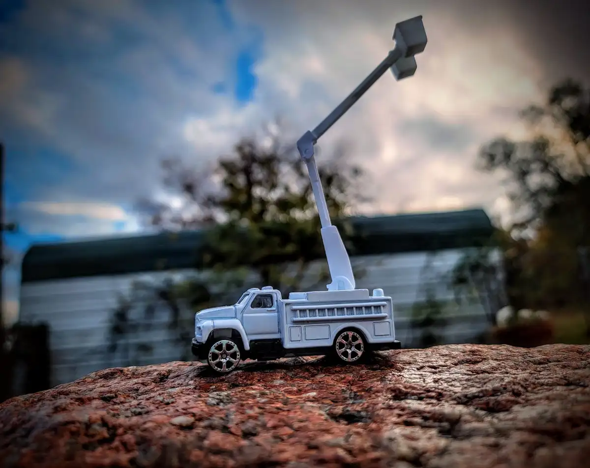 A small white toy utility truck with a crane arm extended upwards sits on a textured reddish-brown rock. The background is…