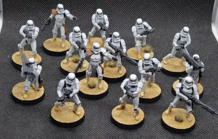 The image shows a collection of painted Star Wars Stormtrooper miniatures, each standing on a circular base with sand and…