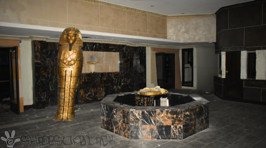 a dimly lit, abandoned hotel lobby features a large golden sarcophagus statue and a central fountain with a golden lid, both…