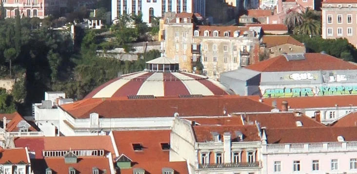An aerial view of a cityscape with red-tiled roofs, featuring a prominent domed building with red and white stripes…