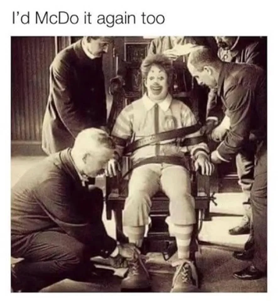 A sepia-toned historical photo shows a man in a clown costume, strapped into a chair, while several men in suits attend to…