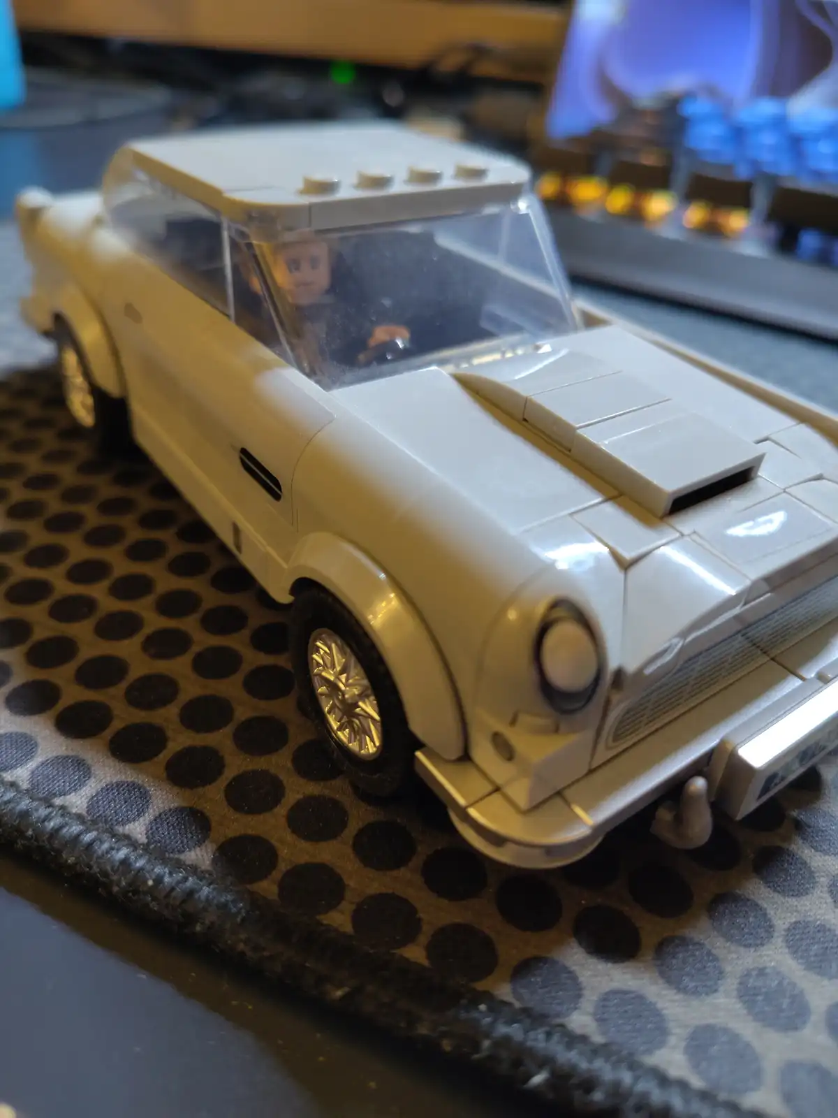 A close-up photo of a white Lego model of a classic car, featuring a Lego minifigure driver inside, resting on a…