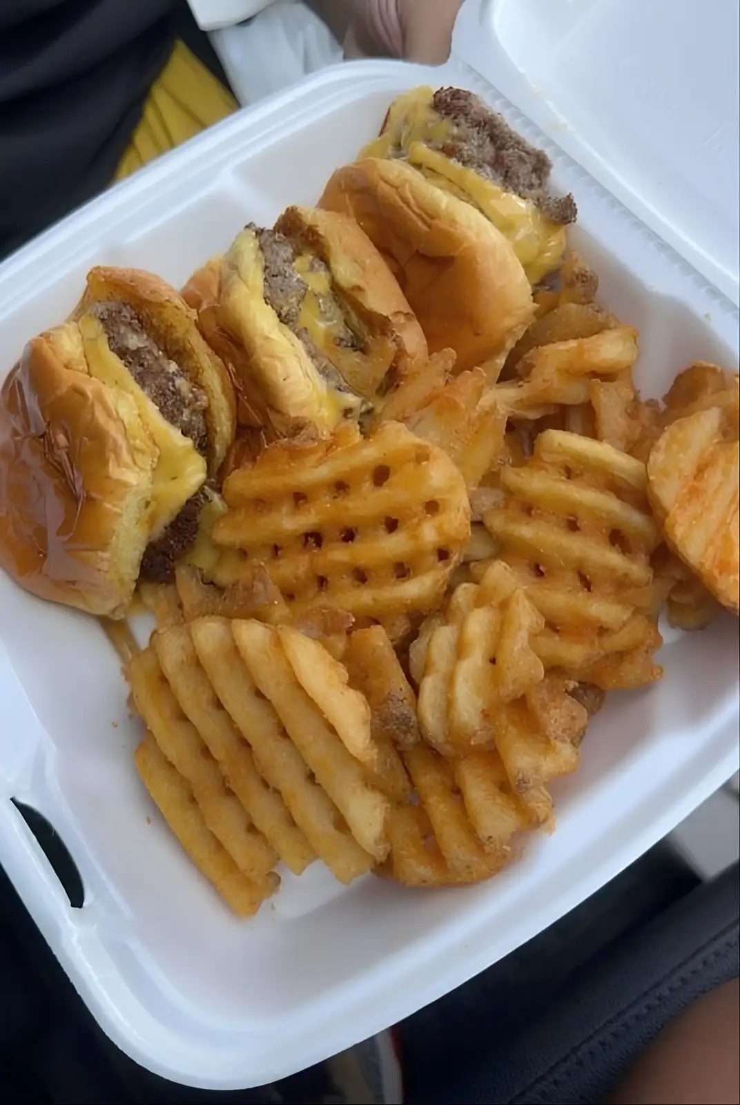 A white styrofoam takeout container holds several cheeseburgers and waffle fries. The text overlaid on the image reads 'i…