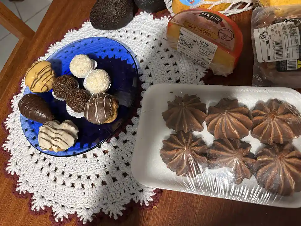 A wooden table holds a blue plate of assorted chocolates and a styrofoam tray of star-shaped chocolates, both resting on a…
