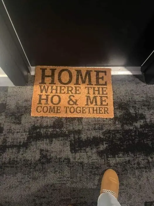 A close-up photo shows a brown doormat on a dark patterned carpet, with the text 'HOME WHERE THE HO & ME COME TOGETHER'…