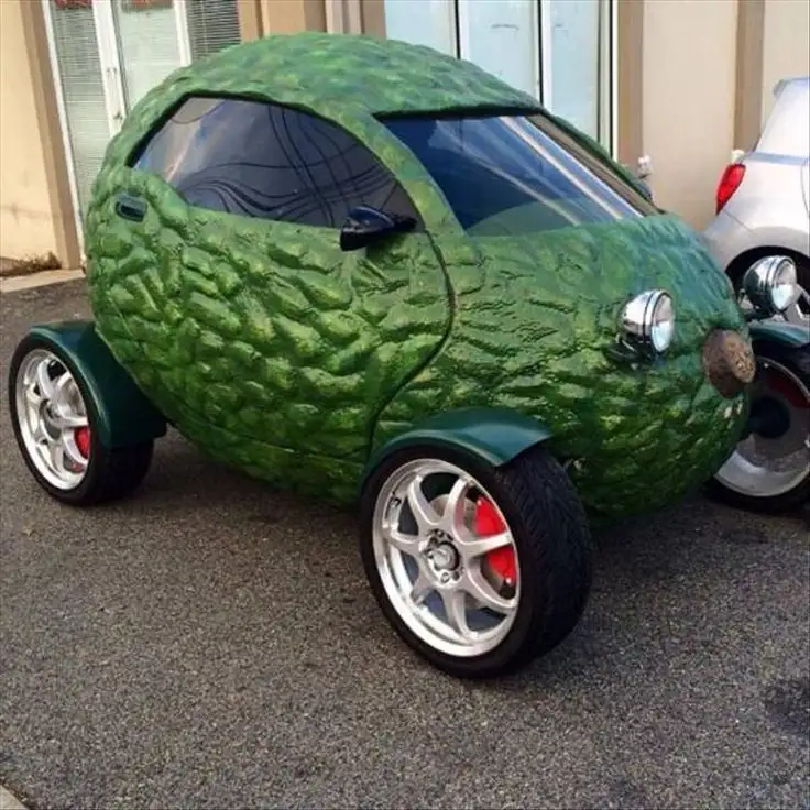 a small, custom-built car is entirely covered in a textured, green, rind-like material resembling a watermelon's outer skin…