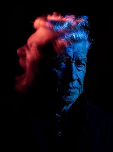 A close-up portrait of an older man with intense eyes, his face split by dramatic lighting: one side bathed in blue, the…