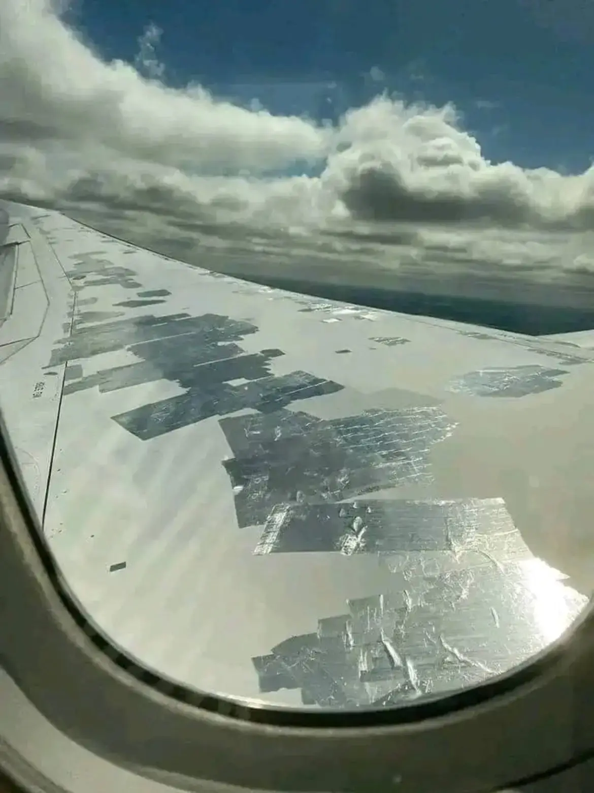 A view from an airplane window shows the aircraft's wing covered in large, irregular patches of what appears to be duct tape…