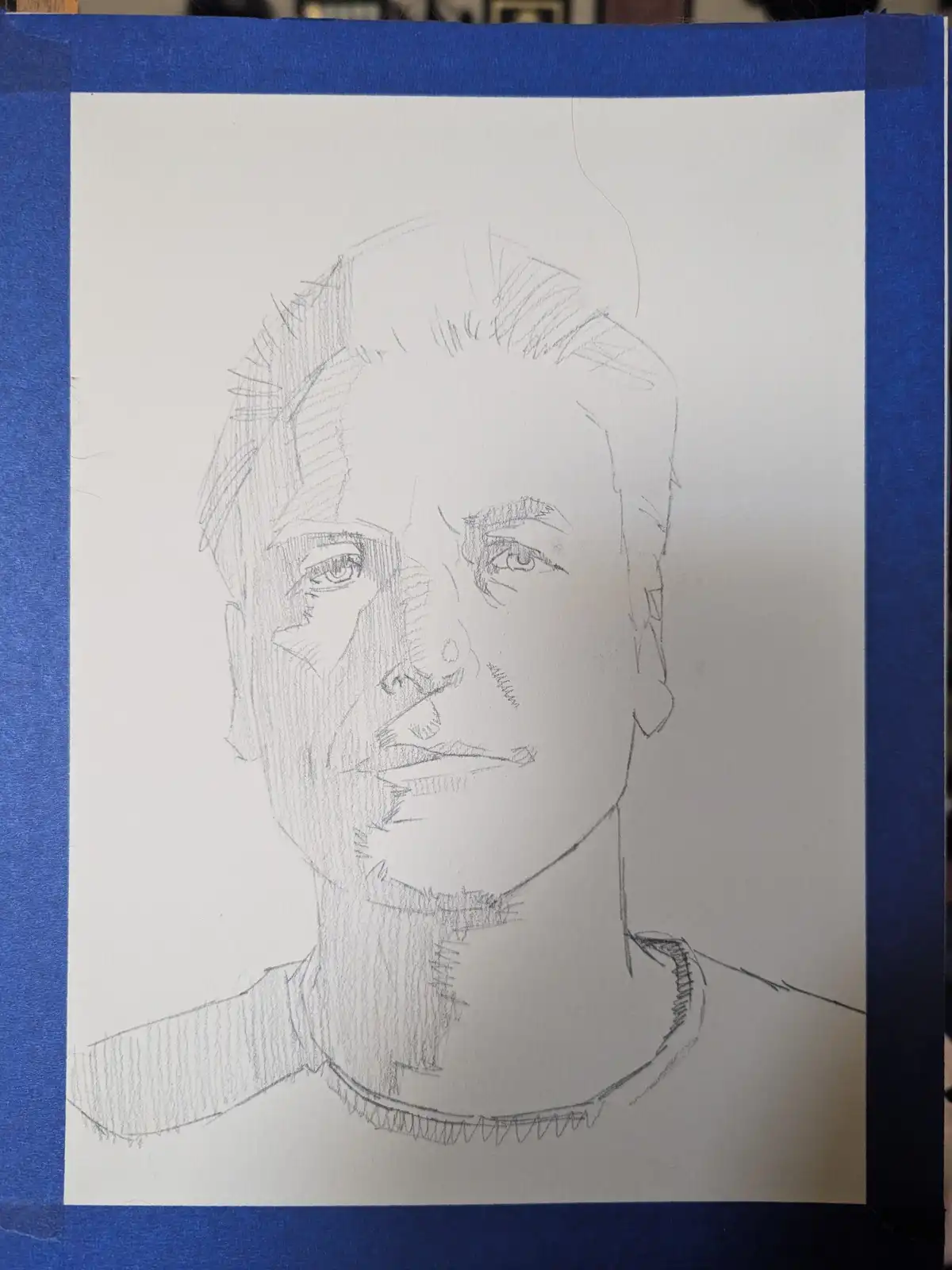 A pencil sketch on white paper taped to a blue surface shows a detailed portrait of a man's face and upper torso. The…