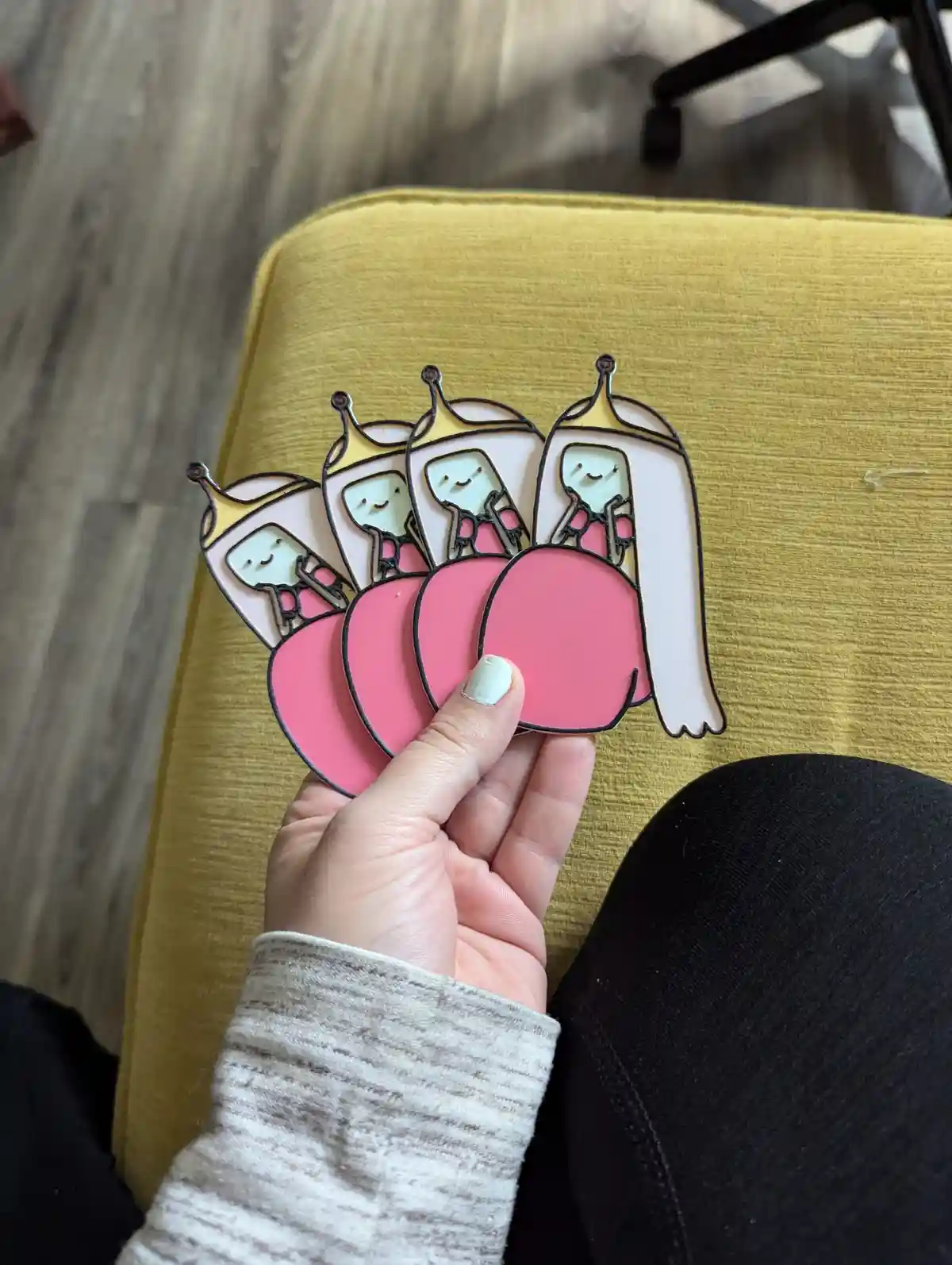 A hand holds four identical enamel pins featuring the character Princess Bubblegum from Adventure Time, each pin showing her…