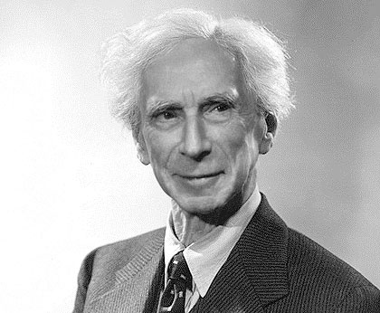 A black-and-white portrait of an older man with white hair, wearing a suit and tie, looking directly at the camera with a…