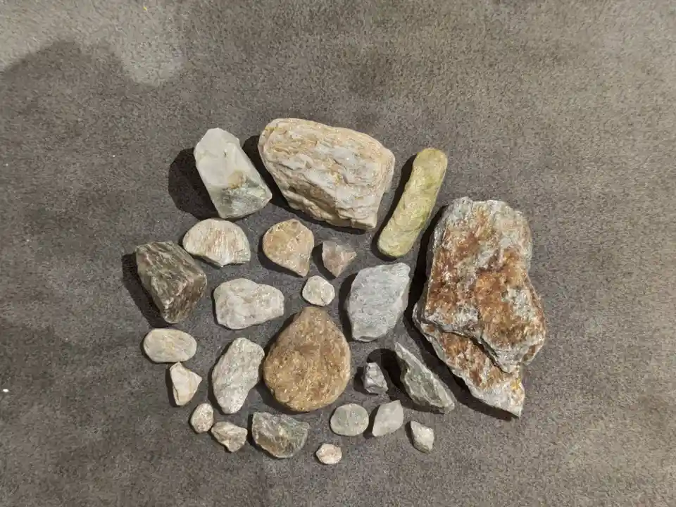 A collection of variously sized and shaped rocks and minerals, mostly gray and beige with some green and rust-colored…