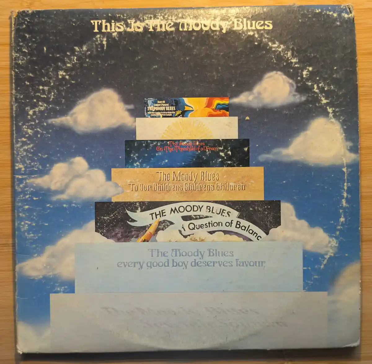 The image shows a heavily worn and scratched album cover for 'This Is The Moody Blues' with a blue sky and clouds…