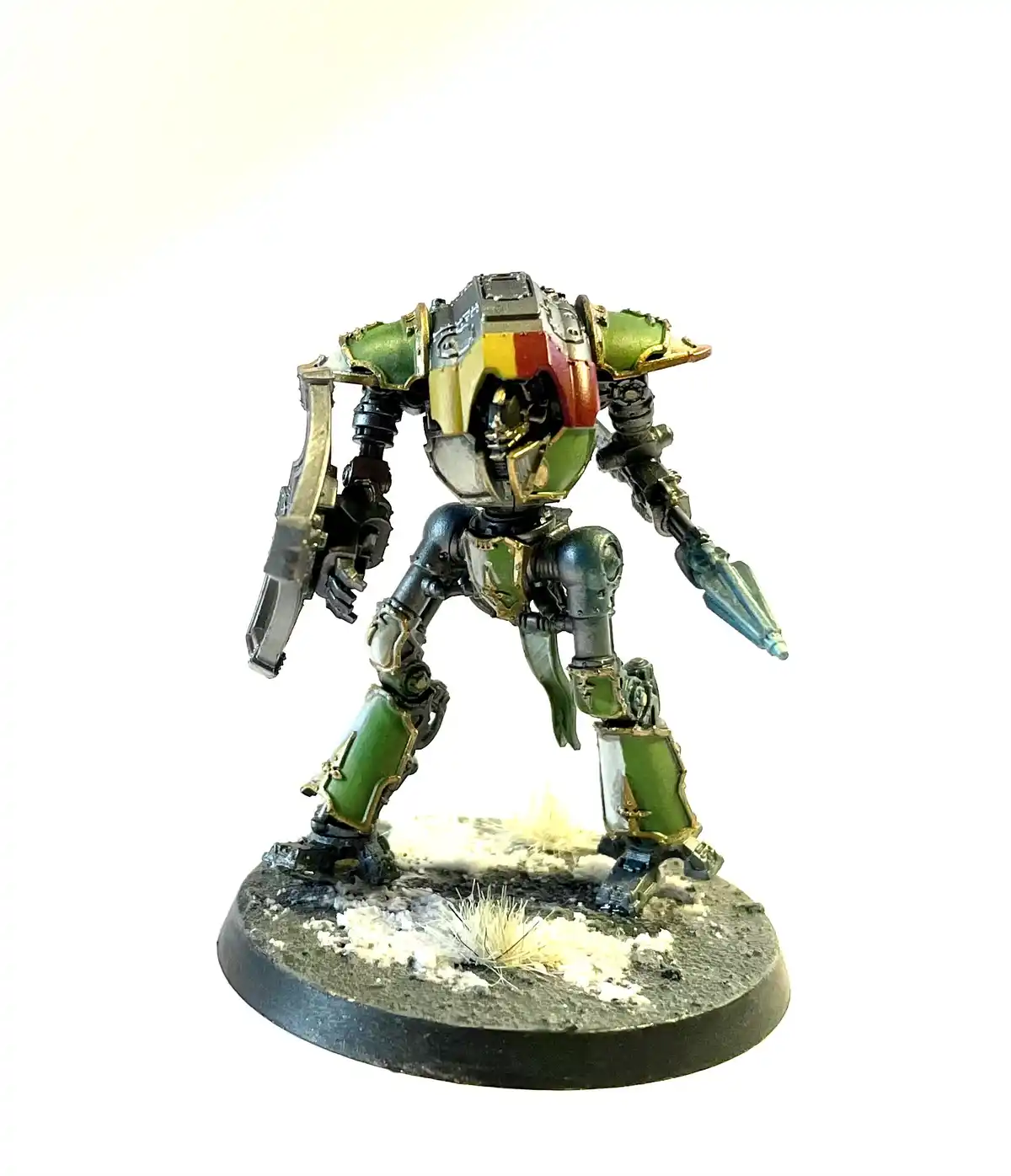 A heavily detailed, painted miniature of a humanoid mech or war machine stands on a circular base with textured terrain. The…