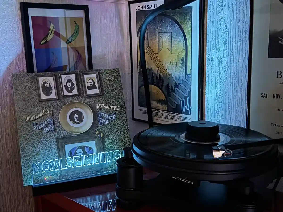 A vinyl record player sits on a table next to a decorative display board featuring framed photos of the band Steele Eye…