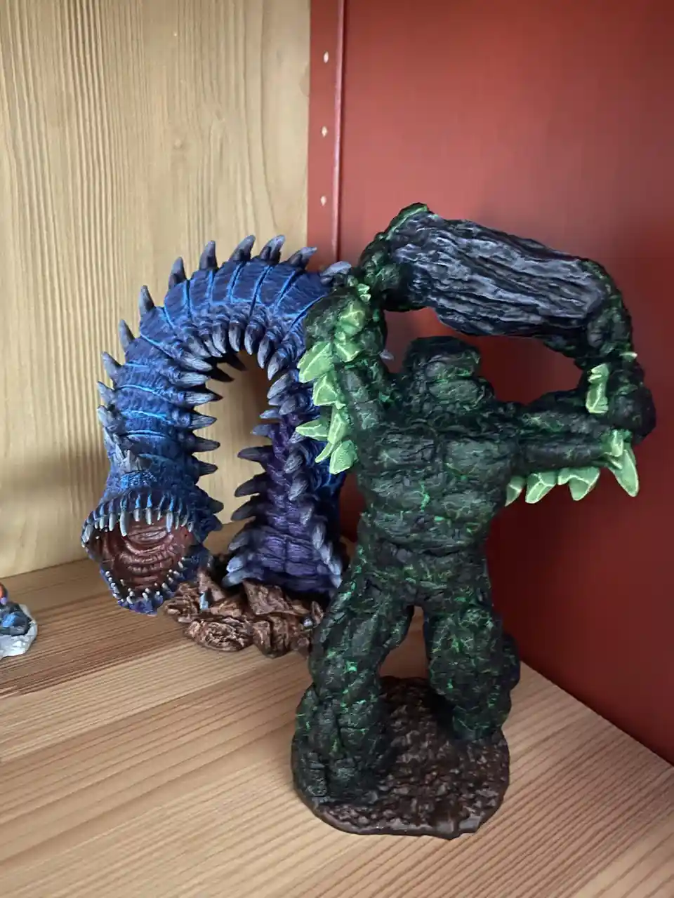 A green, tree-like monster figurine with a large, spiked blue worm-like creature wrapped around its head and neck. The…