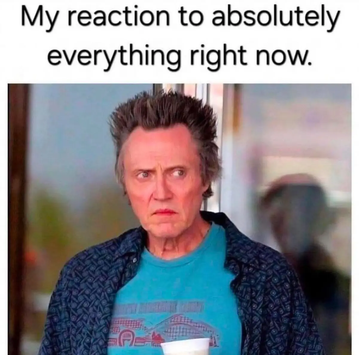 A man with spiky hair, wearing a blue t-shirt under a patterned jacket, stares with a confused and slightly annoyed…