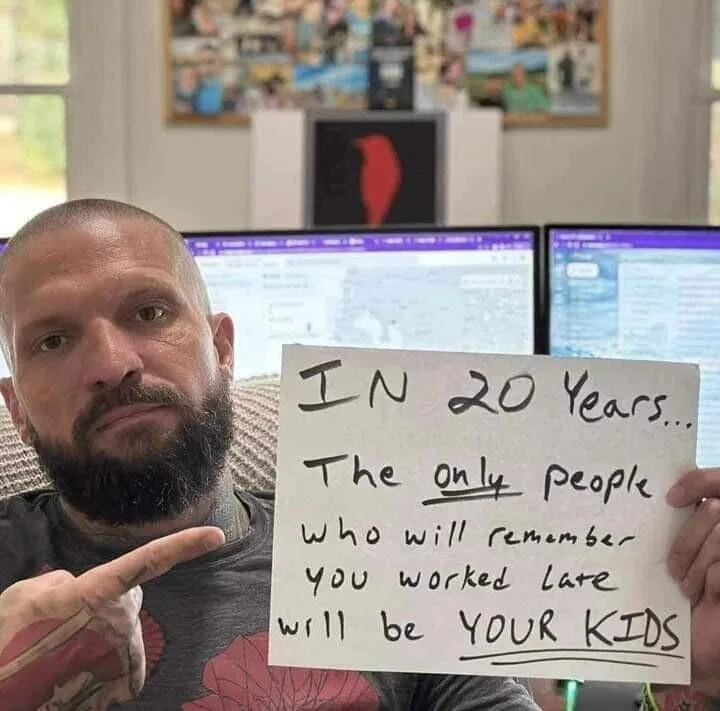 A man with a beard and tattoos points at a handwritten sign he's holding. The sign reads 'IN 20 Years... The only people who…