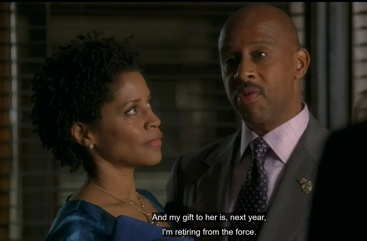 A man in a suit with a police badge pin says he's retiring from the force as a gift to his wife, who looks at him with a…
