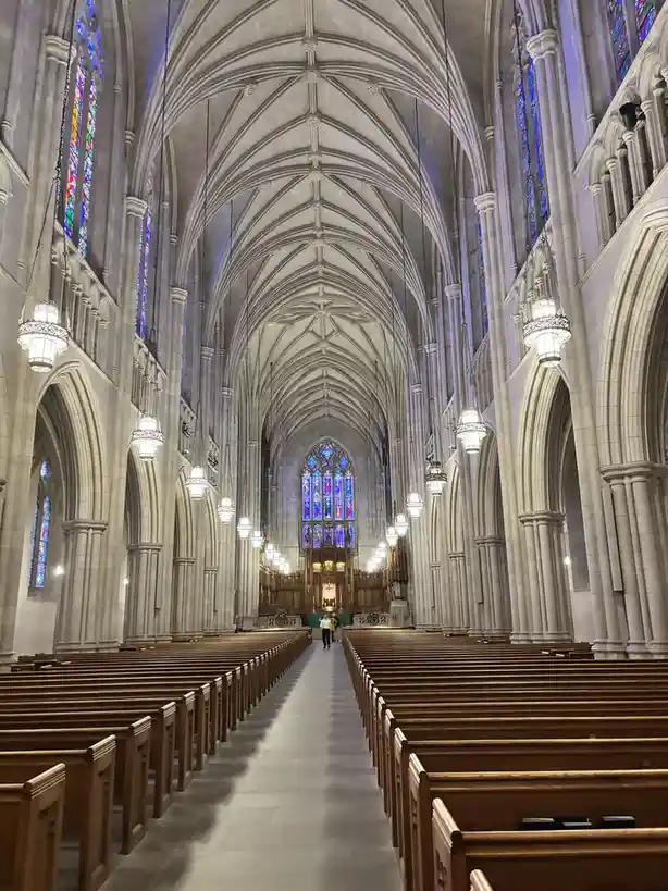 A wide-angle shot of the interior of a grand, empty Gothic cathedral with high vaulted ceilings, stone pillars, and rows of…