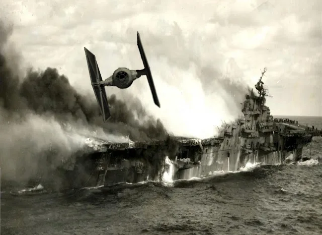 A black-and-white historical photo shows a large naval warship, likely an aircraft carrier, engulfed in flames and smoke…