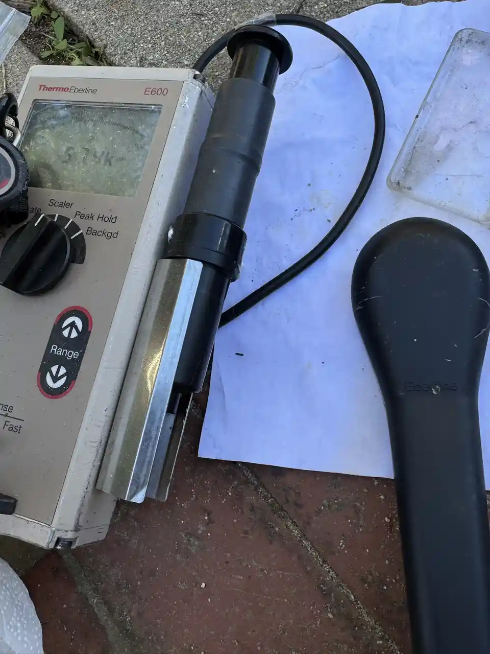 A close-up photo shows a dusty, beige Thermo Eberline E600 radiation detector with its probe attached, resting on a white…