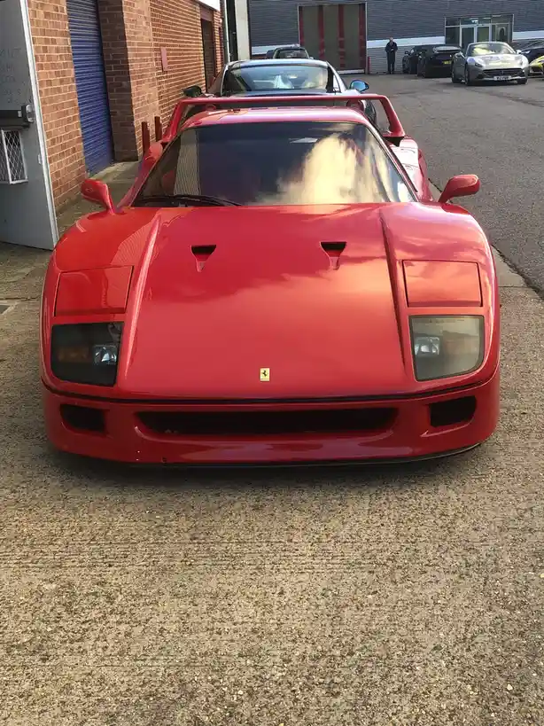 A red Ferrari F40 is parked in a lot with its windshield covered in a large, fluffy cloud of white smoke, obscuring the view…