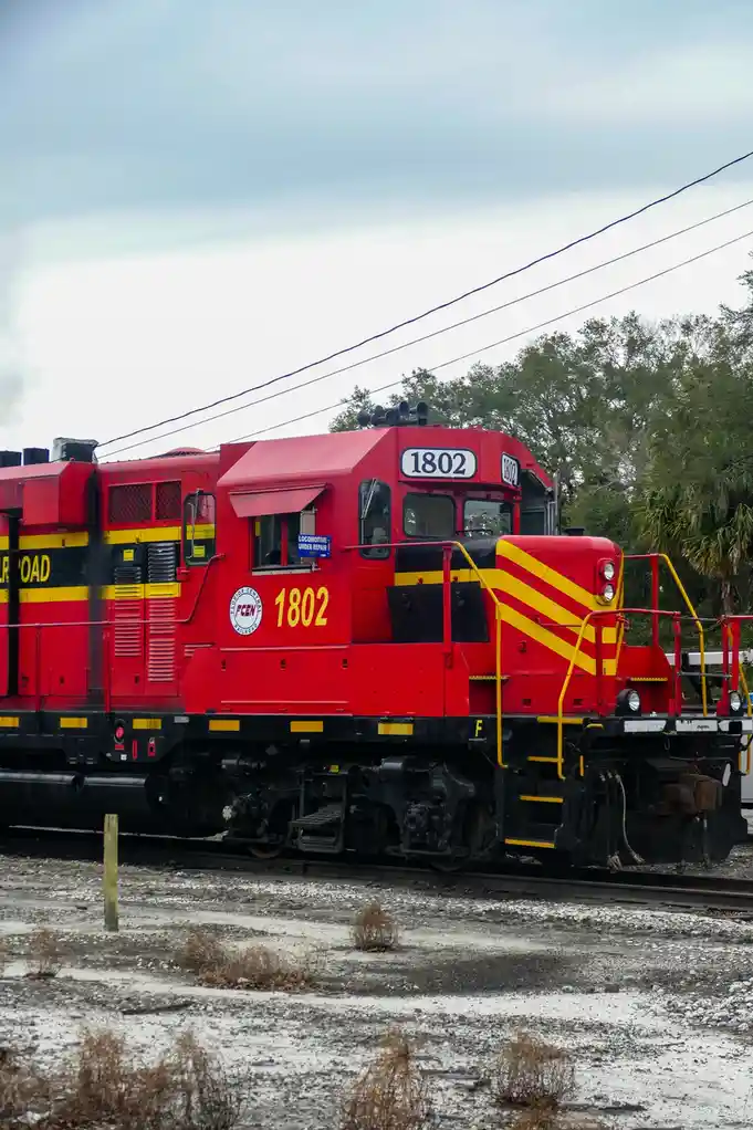A red and yellow Florida Central Railroad locomotive, numbered 1802, is shown on tracks with a blue sign on its side reading…