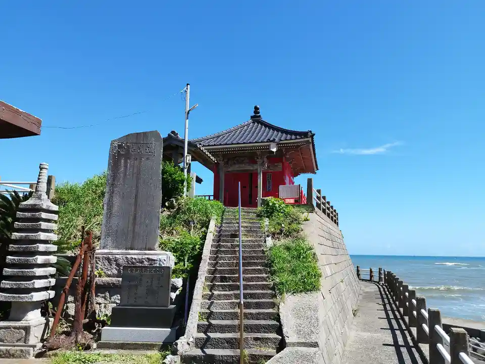a photo of a japanese shrine on a cliffside overlooking the ocean, with stone steps leading up to it, and a large stone…