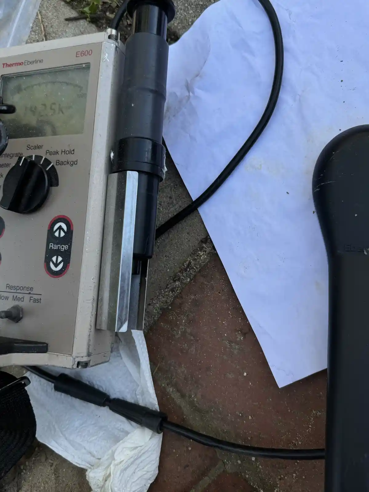 A close-up photo shows a beige Thermo Eberline E600 radiation detector with its digital display reading '142.5k'. The device…