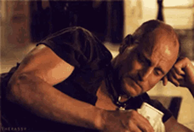 A six-panel sequence shows a bald, muscular man in a dark shirt sitting down, initially looking sad or tired. He then slowly…