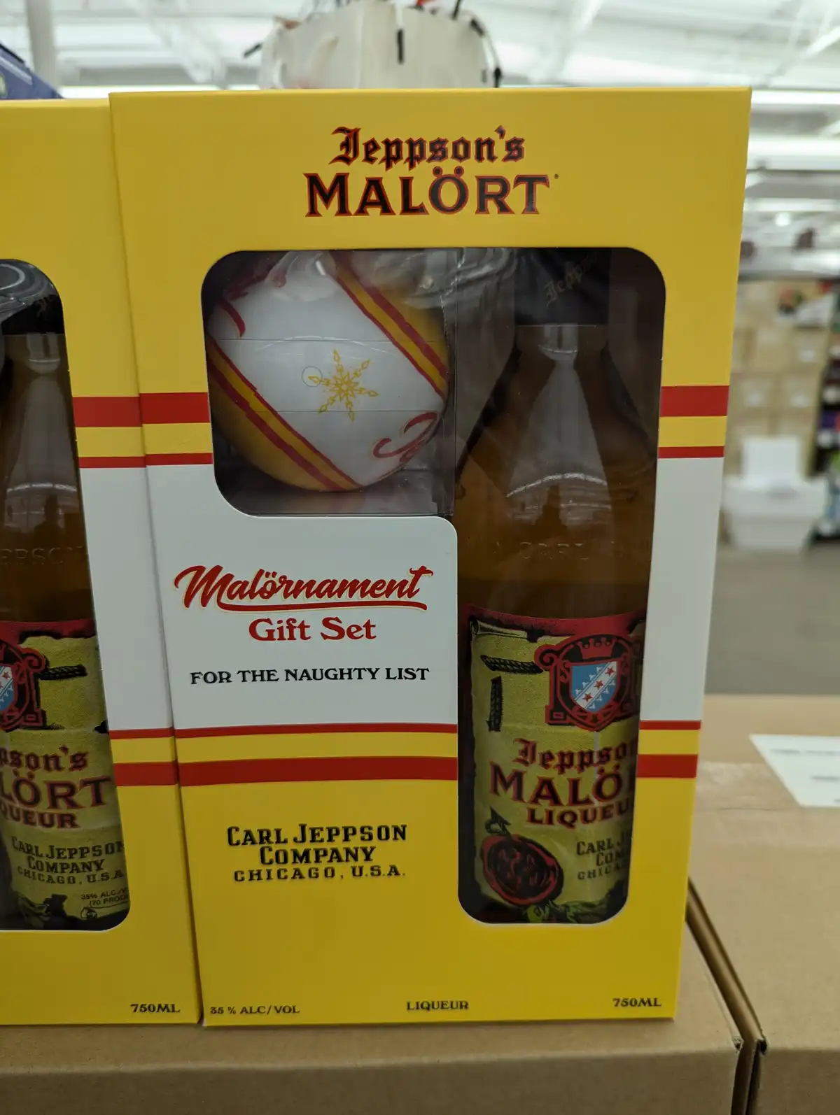 A yellow gift box for Jeppson's Malört liqueur contains a bottle of the alcoholic beverage and a white ornament with red and…