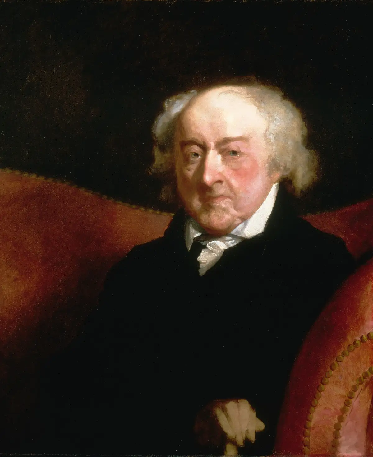 A classical portrait of an elderly white man with white hair, wearing a black coat and white cravat, seated in a red…