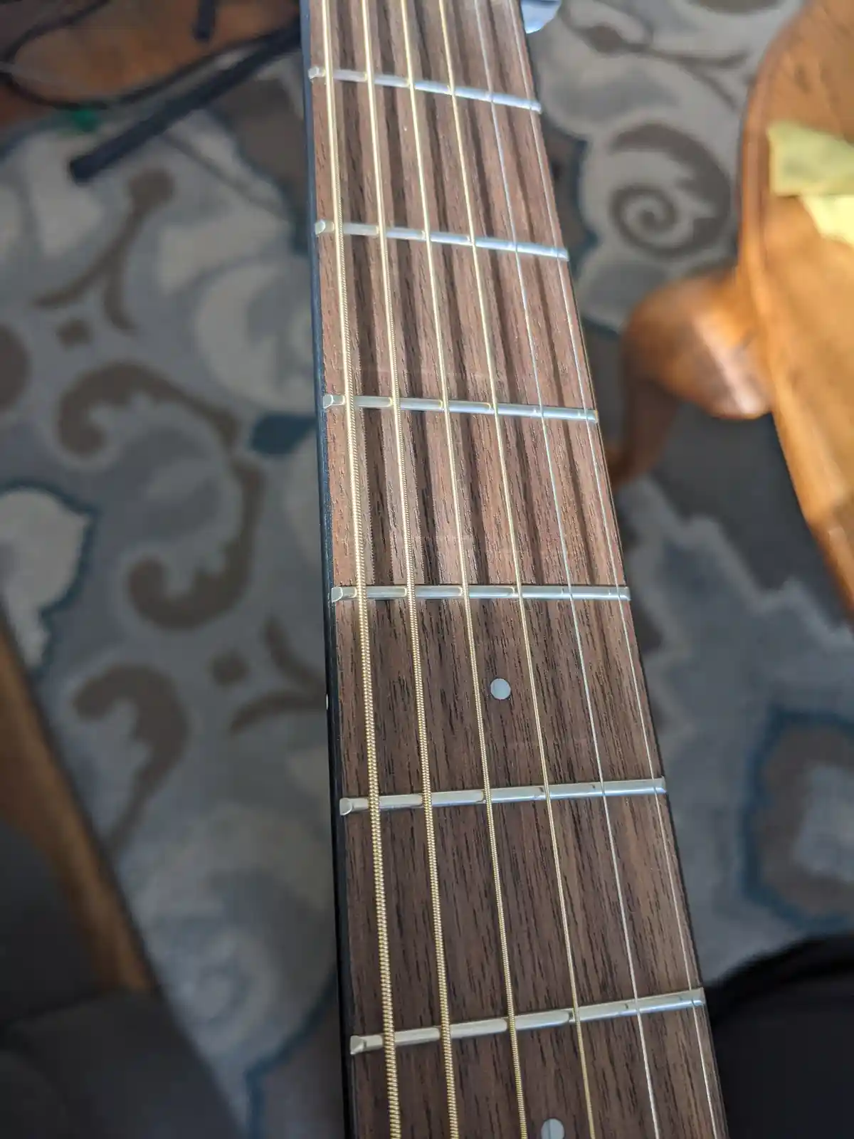 A close-up photo of a guitar's fretboard with dark wood and metal frets, showing the strings and inlays. The overlaid text…