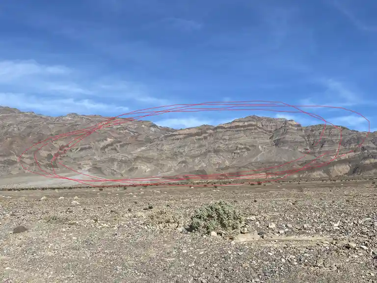 A desert landscape with rocky mountains under a blue sky, overlaid with multiple red hand-drawn lines forming an oval shape…