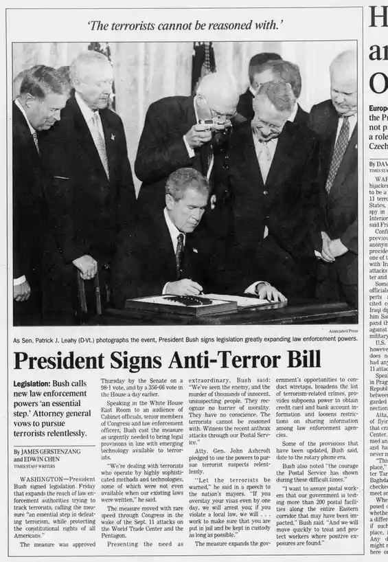 A black-and-white newspaper clipping shows President George W. Bush signing an anti-terror bill while surrounded by…