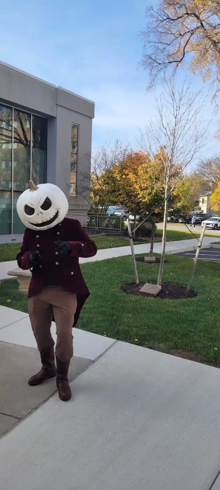 A person dressed as Jack Skellington from The Nightmare Before Christmas, wearing a white pumpkin head with stitched eyes…