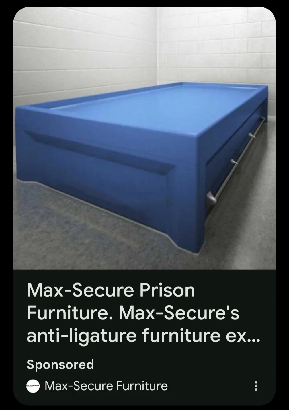 A blue, solid, boxy prison bed with no visible gaps or openings sits in a stark, white-tiled cell. Overlaid text mimics a…